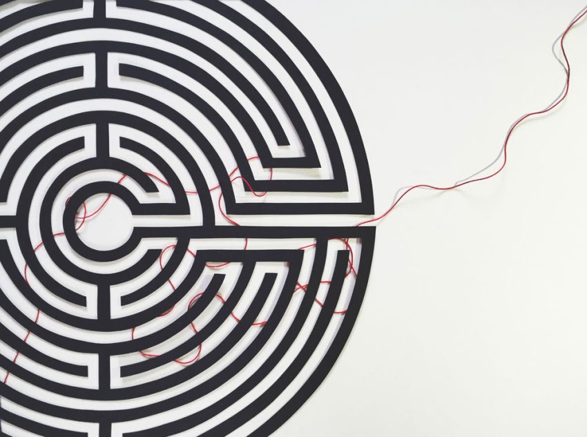 A close-up scene of a hand unspooling a red thread across stone corridors, clearly marking a navigable path through the maze.